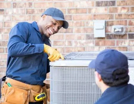 Two technicians inspecting the top of an outdoor HVAC condenser