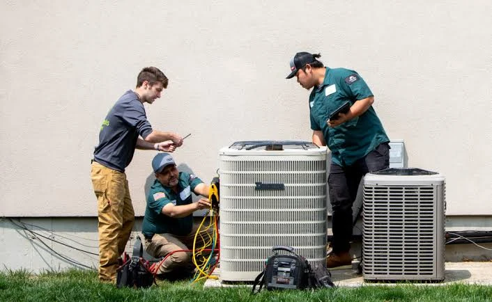 Three HVAC technicians working on residential outdoor condenser units
